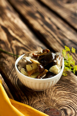 Marinated mushrooms in glass jar, herbs and spices on wooden table. Canned vegetatian dish. Natural light. Selective focus.