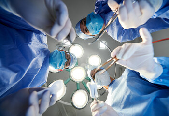 View from below of doctors holding medical instruments during plastic surgery. Team wearing...