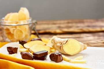 Candied ginger slices in dark chocolate on a white plate on wooden table. Dehydrated oriental...