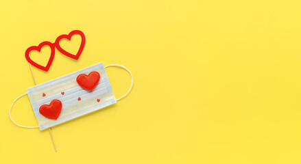 New normal Valentine's Day concept. Medical face mask decorated with red hearts and party accessories glasses on Illuminating yellow background. Top view, Copy Space, minimalism. Creative flat lay