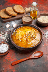 bottom view chicken soup bowls with pepper rice sea salt garlic spoon oil bread slices on cutting board on dark red background