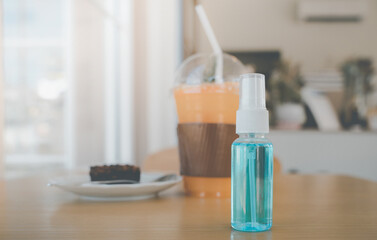 bottle of blue alcohol spray with blurred beverage in coffee shop , necessary for new normal lifestyle after loose covid-19 lockdown, vintage tone