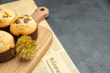 Half shot of freshly baked small cupcakes with accessories on wooden cutting board on newspaper on dark background