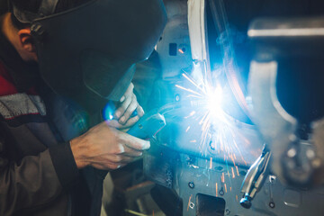 Professional car body repair, welding of auto body. Industrial worker welds metal elements of...