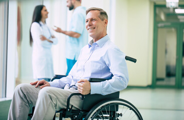 Obraz premium Senior handsome man in a wheelchair is moving in the hospital with help of medical special staff