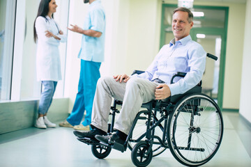 Obraz premium Senior handsome man in a wheelchair is moving in the hospital with help of medical special staff