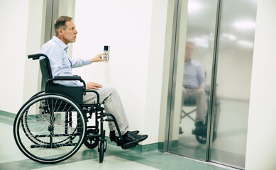 Ill senior man in a wheelchair is pushing on the button for call elevator in the hospital