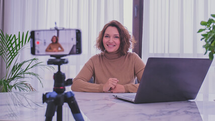 Smiling woman recording her video blog. Woman blogger videotapes her vlog at home.  Adult woman...