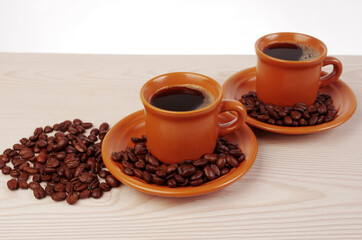 Two brown cups of coffee and coffee beans on a wooden table.