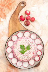 Vertical view of delicious chicken salad with beet served with chopped red radishes on a gray plate on wooden cutting board on mixed color background image