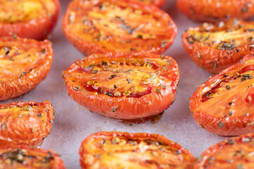 Roasted tomatoes are lined up on a baking sheet covered in spices