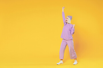 Full length of young blonde caucasian woman 20s bob haircut in casual basic purple suit beanie hat doing winner gesture clenching fists saying yes isolated on yellow background studio portrait.