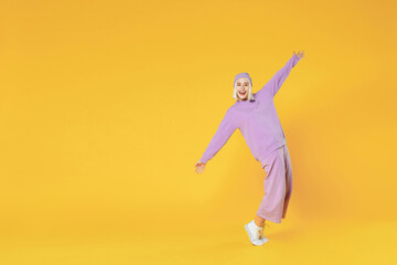 Full length young blonde caucasian woman bob haircut wearing casual basic purple suit beanie hat dancing standing on toes spreading hands fooling around isolated on yellow background studio portrait