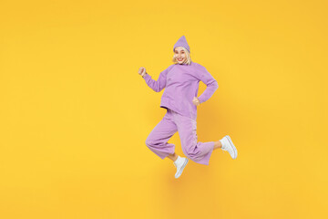 Fototapeta na wymiar Full length of young caucasian excited fun woman 20s in casual basic purple suit beanie hat side view running jumping clenching fists look camera isolated on yellow color background studio portrait.
