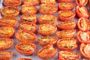 Roasted tomatoes are lined up on a baking sheet covered in spices