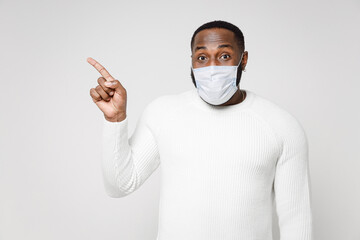 Young african american man in basic sweater sterile face mask safe from coronavirus virus covid-19 during quarantine pointing index finger aside up isolated on white color background studio portrait.