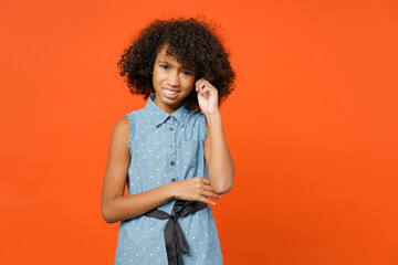 Puzzled tired little african american kid girl 12-13 years old wearing casual denim dress put hand on head isolated on orange color background children studio portrait. Childhood lifestyle concept.