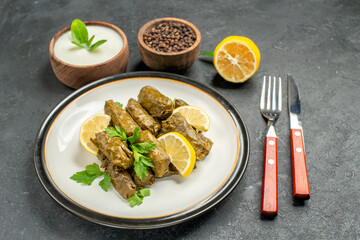 bottom view azerbaijani cuisine dolma on white oval plate bowls with natural yogurt black pepper a slice of lemon knife and fork on dark background