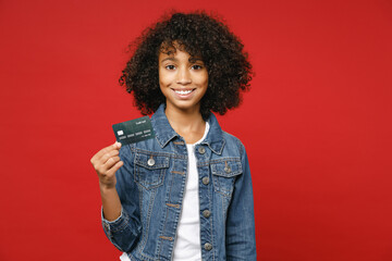 Smiling pretty little african american kid girl 12-13 years old in denim jacket hold credit bank...