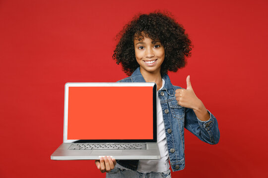 Funny Little African American Kid Girl 12-13 In Denim Jacket Hold Laptop Pc Computer With Blank Empty Screen Showing Thumb Up Isolated On Red Background Children Portrait. Childhood Lifestyle Concept.