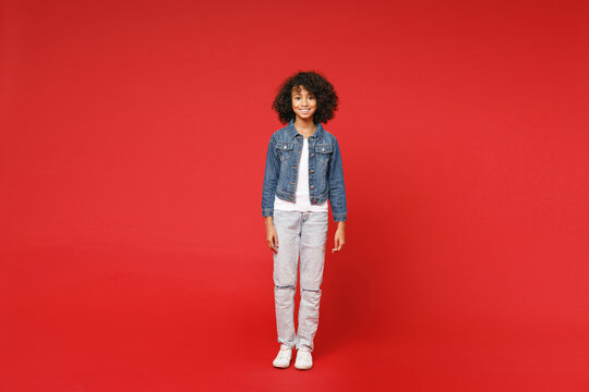 Full length of smiling little african american kid girl 12-13 years old in casual denim jacket looking camera isolated on bright red background children studio portrait. Childhood lifestyle concept.