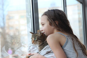Smiling cute girl with domestic cat looking through the window