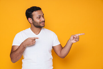 Asian young unshaven man pointing his fingers aside at copyspace