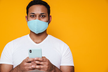 Asian man in face mask using mobile phone and looking at camera