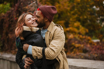 Multinational happy couple hugging and making fun at city street