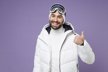 Smiling skier man in warm windbreaker jacket ski goggles mask showing thumb up going to spend extreme weekend winter season in mountains isolated on purple background. People lifestyle hobby concept.