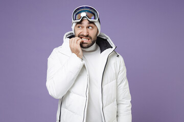 Nervous worried skier man in white windbreaker jacket ski goggles mask gnawing nails spend extreme...