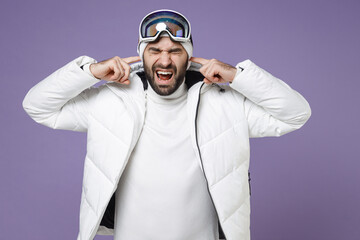 Crazy skier man in white windbreaker jacket ski goggles mask cover ears with fingers screaming spend extreme weekend winter in mountains isolated on purple background. People lifestyle hobby concept.