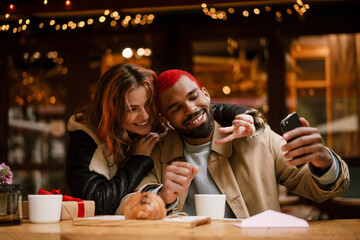 Multinational happy couple taking selfie together in cafe outdoors