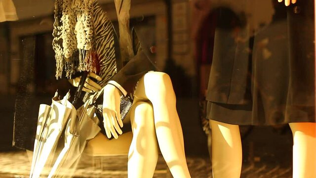 Pair of mannequins, women. One sitting, one standing in a showcase.