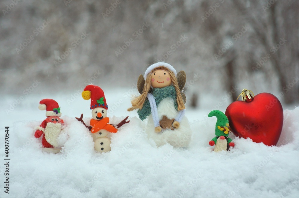 Wall mural Figurine of santa claus, snowman and gnome on a background of snow. Nearby there is a Christmas angel. Fairy-tale characters in the winter forest.