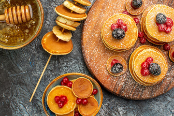 Close up view of American pancakes on cutting board and honey with spoon on gray table