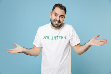 Confused puzzled young bearded man in white volunteer t-shirt spreading hands looking camera...