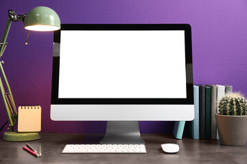 Comfortable workplace with modern computer and cactus on table near purple wall. Space for design