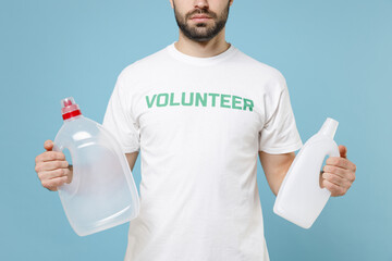 Cropped image of young man in white volunteer t-shirt hold plastic bottles trash isolated on blue color background studio portrait. Voluntary free assistance help trash sorting recycling concept.