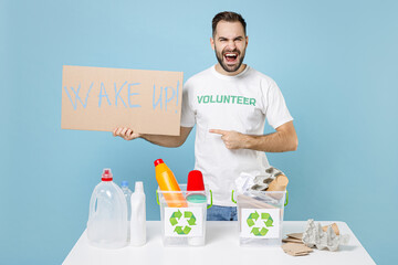 Screaming man in volunteer t-shirt stand near recycling stations sorting plastic paper trash point nameplate wake up isolated on blue background. Voluntary free work assistance help charity concept.