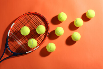 Tennis racket and balls on orange background, flat lay. Sports equipment