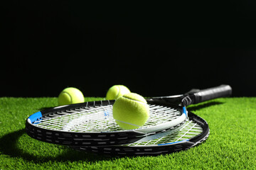 Tennis rackets and balls on green grass against dark background. Space for text