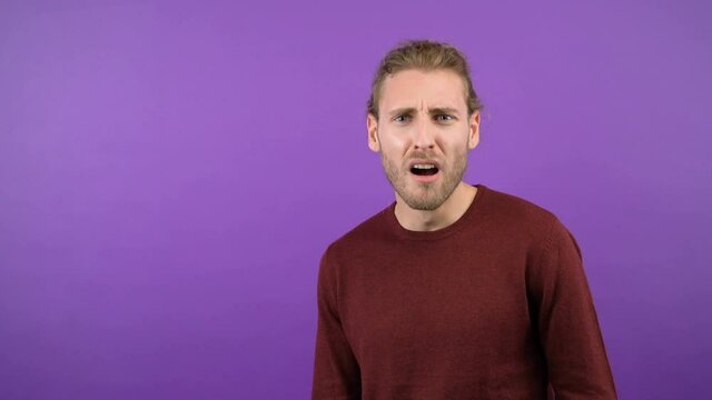 Waist-length portrait of a pleasant surprised cheerful man looking at the camera. Young long-haired hipster isolated on purple background. 4K