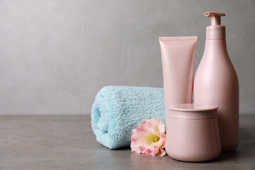 Different hair products, towel and flower on grey table. Space for text