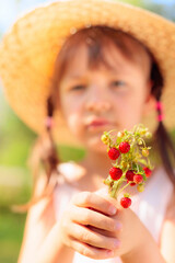 Little girl holding wild strawberry in hand.
