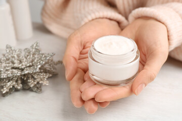 Woman holding jar of cream at light table, closeup. Cosmetic product for winter
