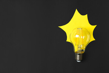 Lamp bulb with yellow paper imitating light on black background, flat lay