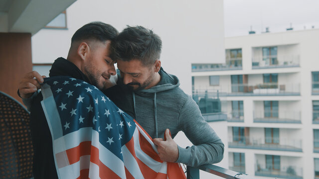 Happy handsome gay couple hugging under USA flag on the balcony. High quality photo - Powered by Adobe