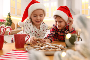 Cute little children taking tasty Christmas cookies from plate at  table in kitchen