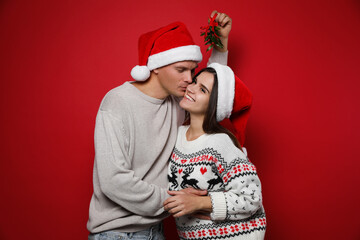 Fototapeta premium Happy couple under mistletoe bunch on red background